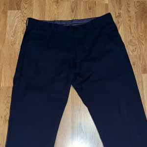 Mörkblå kostymbyxor från Riley - Snygga mörkblå kostymbyxor från Riley i slim fit-modell. Byxorna har klassisk design med hällor för bälte, diskreta bakfickor och stängs med knapp och dragkedja. Perfekta för en dressad look. De är köpa på brothers. I med kavaj. Tillsammans gick kostymen för 2000kr. Generösa priset beror på att byxorna är för stora för mig, då jag under perioden jag köpte dem ville ha baggy byxor, så köpte för långa/breda. Har 48 egentligen.