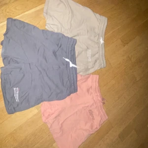 Tre par mjuka shorts i olika färger - Tre par bekväma shorts i bomull, perfekta för sommaren. Ett par är beige, ett par är grå och ett par är ljusrosa. Alla har elastisk midja och kort modell. Passar till avslappnade dagar eller träning.