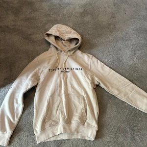 Beige hoodie från Tommy Hilfiger - Säljer en beige hoodie från Tommy Hilfiger med klassisk logga på bröstet.  Från äkta märket.