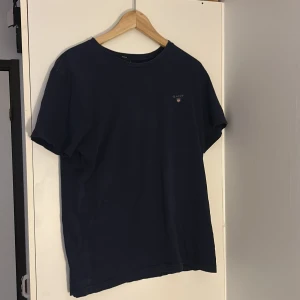 Mörkblå t-shirt från GANT - Säljer en stilren mörkblå t-shirt från GANT i bomull. T-shirten har rund halsringning, korta ärmar och en liten broderad logga på bröstet. Perfekt för en enkel och klassisk look.