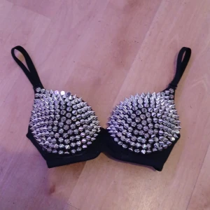 Nitt bh Svart bh-topp med nitar - Cool svart bh-topp täckt med silvriga nitar över hela framsidan. Justerbara axelband och stadig passform. Perfekt för dig som vill sticka ut och skapa en edgy look.