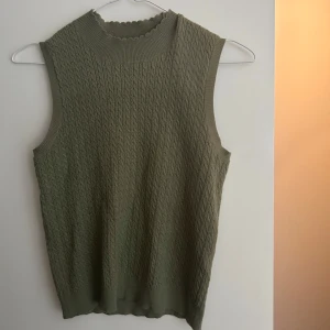 Olivgrön stickad väst från Zara - Olivgrön stickad väst från Zara med ribbad, vågig halsringning. Västen är ett set tillsammans med kjolen (kjolen säljs separat)