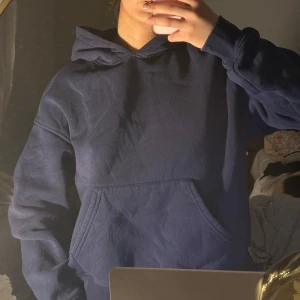 Mörkblå hoodie med ficka - Säljer en enkel och stilren mörkblå hoodie med huva och stor magficka. Tröjan har långa ärmar och en avslappnad passform, perfekt för vardagsbruk eller när du vill vara extra bekväm.