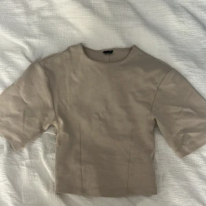 Beige kortärmad topp - Säljer en stilren beige topp med korta ärmar och rund halsringning. Toppen har en rak passform och är tillverkad i ett mjukt material som känns skönt mot huden. Perfekt att matcha med jeans eller kjol.