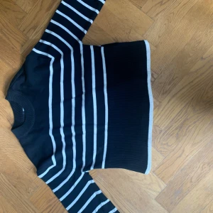 Svart och vit randig stickad tröja från Gina Tricot - Säljer en svart stickad tröja från Gina Tricot med vita horisontella ränder. Tröjan har lång ärm och ribbad mudd vid hals, ärmslut och nederkant. Perfekt för kyligare dagar och enkel att matcha med jeans eller kjol.