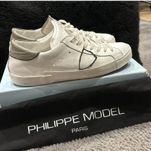 Philippe model skor - Snygga vita sneakers från philippe model med oliv hröna detaljer. Skorna har en stilren design och är mycket trendiga just nu. Box och dustbag tillkommer även. Hör av er vis funderingar