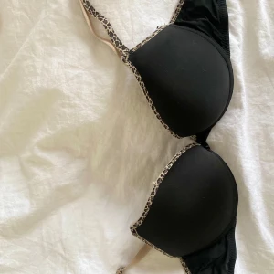 Svart bh med leopardmönstrade detaljer från H&M - Säljer en svart bh från H&M med snygga leopardmönstrade kanter och axelband. Bh:n har vadderade kupor och justerbara axelband för bästa passform. Ena bandet har gått sönder men det går att sy fast. Perfekt för dig som vill ha något både bekvämt och trendigt.