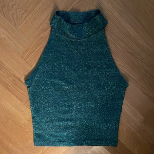 Grön glittrig polotopp från Gina Tricot - Säljer en grön glittrig polotopp från Gina Tricot i storlek XS. Toppen är ärmlös med hög krage och har en snygg, figurnära passform. Perfekt till fest!