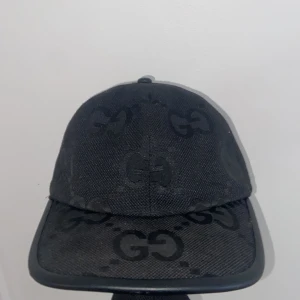 Svart keps från Gucci med GG-mönster - Säljer en svart keps från Gucci med det klassiska GG-mönstret ton-i-ton över hela kepsen. Kepsen har böjd skärm och justerbar passform. Tillverkad i Italien och har en exklusiv känsla.