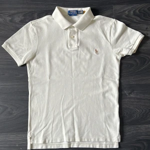 Beige piké från Polo Ralph Lauren - Klassisk beige pikétröja från Polo Ralph Lauren med broderad logga på bröstet. Slim fit-modell med korta ärmar, krage och knappar framtill. Perfekt för en stilren och tidlös look. Skicka gärna prisförslag eller skriv vid frågor!!