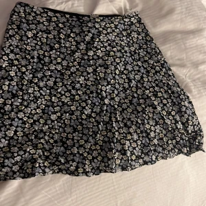 Blommig kortkjol från hm - Säljer en svart kortkjol från Divided med blommigt mönster i vitt och grått. Kjolen har en lätt utsvängd form och är perfekt för dig som gillar en feminin och trendig stil. Resår i midjan för extra komfort.