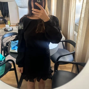 Svart volangklänning med puffärmar - Säljer en svart kortklänning med långa puffärmar och volangdetaljer nertill. Klänningen har rynkade partier framtill som ger en snygg form och en trendig look. Perfekt för dig som vill sticka ut med en stilren men ändå lekfull outfit.