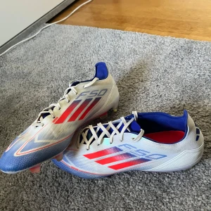 Adidas F50 elite fotbollsskor  - Säljer ett par Adidas F50 fotbollsskor i vitt med blå och röda detaljer. Använda ett par gånger, men fortfarande i väldigt bra skick. Storlek 42 2/3.