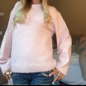 Ljusrosa stickad tröja - Mysig ljusrosa stickad tröja med rund halsringning och långa ärmar. Tröjan har en avslappnad passform och ribbade muddar vid ärmslut och nederkant. Perfekt för lager-på-lager och enkel att matcha med jeans eller kjol.