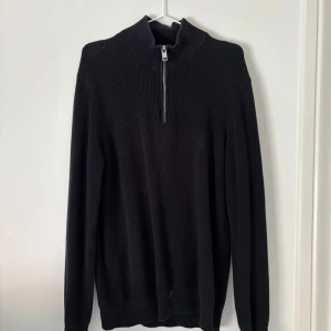 Svart stickad tröja med dragkedja - Svart stickad tröja med dragkedja framtill. Långärmad modell med ribbad struktur. Använd ett fåtal gånger och har en fläck men får bort i tvätten! 