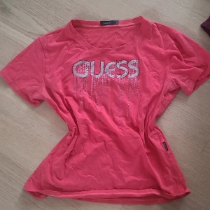 Rosa t-shirt med strass från Guess - Snygg rosa t-shirt från Guess med korta ärmar och glittrande strassdetaljer som bildar loggan på bröstet. Inga stenar har trillat av. Står att den är i storlek XXL men är inte ett dugg för stor för mig i stl S. Aldrig använd.