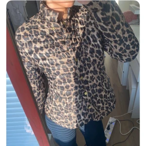 Leopardmönstrad pufferjacka med guldknappar - Säljer en snygg pufferjacka med leopardmönster och guldiga knappar. Jackan har hög krage, långa ärmar och praktiska fickor. Perfekt för dig som vill sticka ut med en trendig look.