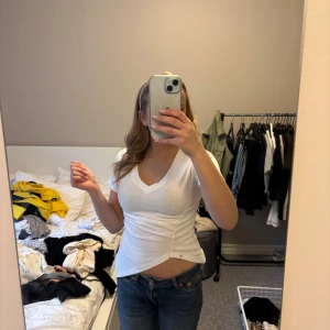 Vit v-ringad t-shirt med asymmetrisk nederkant - Säljer en vit t-shirt med v-ringning och korta ärmar. Toppen har en snygg asymmetrisk nederkant som ger en unik look. Perfekt att styla med jeans eller kjol för en trendig outfit.