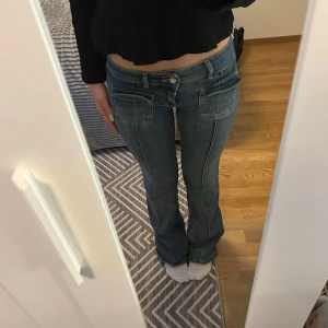 Blå jeansbyxor från Nelly med fickdetaljer - Säljer ett par blå jeansbyxor från Nelly med låg midja och raka ben. Byxorna har stora fickor framtill, dubbla knappar och dragkedja.