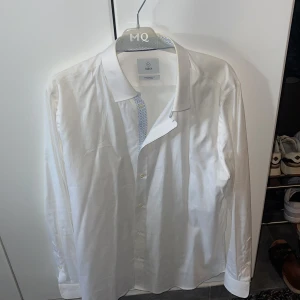 Vit skjorta från MQ - Klassisk vit skjorta från H&M med lång ärm och knappar framtill. Skjortan har en stilren design och är tillverkad i bomull, perfekt för en clean och fräsch look.