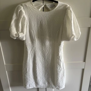 Vit klänning med puffärm  - Superfin vit klänning från Vila med puffärmar och fint blommigt mönster. Figursydd passform och med en snygg öppen rygg! Perfekt för sommarens tillfällen, så som studenten och midsommar mm! Det har blivit en liten sminkfläck vid halsen (se sista bilden) men den syns knappt, men är därav öppen för prisförslag. Köpt för 599kr