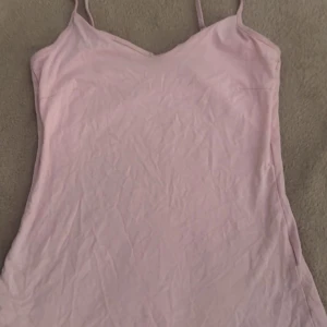 Ljusrosa linnetopp från 157 XS - Supersöt ljusrosa linnetopp från 157 i storlek XS. Tunt och mjukt material i bomull, med smala axelband och enkel, rak passform. Perfekt att styla med jeans eller kjol för en chill look. Färgen är riktigt fin och passar till allt!