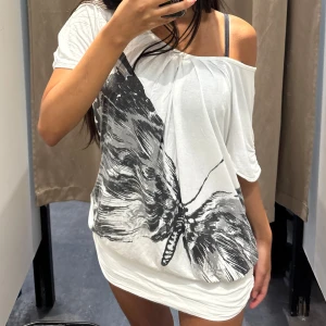 Vit kortklänning med fjärilstryck - Superfin vit kortklänning med stort svart fjärilstryck framtill. Klänningen har en lös passform, offshoulder och öppen rygg som ger en cool vibe. Tunt och mjukt material, perfekt för varma dagar eller när du vill sticka ut. Storlek är L men passar mig som är S