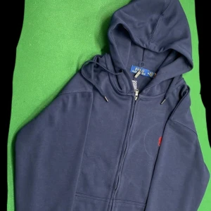 Marinblå hoodie från Polo Ralph Lauren - Snygg marinblå hoodie från Polo Ralph Lauren med dragkedja och huva. Tröjan har snörning vid huvan och klassisk röd logga broderad på bröstet. Tillverkad i 100% bomull för en skön och avslappnad känsla. Pris kan diskuteras!! 