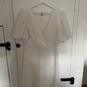 Vit omlottklänning från NLY Trend - Vit kortklänning från NLY Trend med omlott framtill och puffiga korta ärmar. Stängs med hjälp av kedja på sidan (bild 4). Hade band så man kunde knyta runt klänningen först men har klippt bort det. Använd två gånger.
