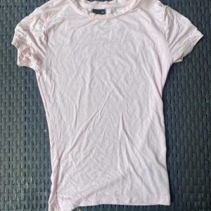 Ljusrosa t-shirt från Gina Tricot - En basic ljusrosa t-shirt från Gina Tricot i mjuk bomull. Modellen är klassisk med rund halsringning och korta ärmar. Perfekt att matcha med jeans eller kjol för en enkel och fräsch look. Sparsamt använd.