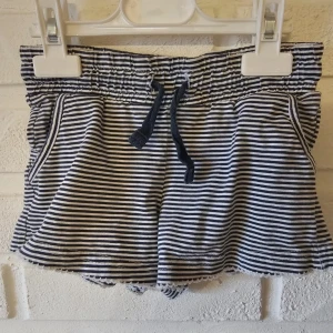 Randiga shorts med snörning Casual Girls - Superfina shorts från Casual Girls i svartvitt randigt mönster. De har elastisk midja med snörning och söta spetsdetaljer längst ner. Perfekta för varma dagar och riktigt sköna tack vare mjukt bomullsmaterial. Lätt tvättpåverkade 