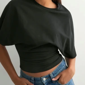 Svart croppad topp med vida ärmar - Säljer en svart croppad topp med bred resår i midjan och oversized, korta ärmar. Den är från Nelly och är helt ny med lappen kvar. Toppen har en enkel och clean look med rund halsringning och är tillverkad i mjuk bomull. Perfekt för dig som gillar en avslappnad men ändå trendig stil.