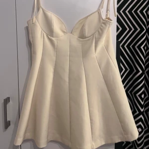 Champagnefärgad kort klänning från Zara - Supersöt kort klänning från Zara i champagnefärg med smala axelband och markerad byst. Klänningen har en lätt utsvängd kjol och dold dragkedja i ryggen. Perfekt för sommar