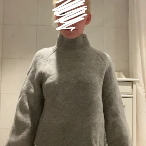 Grå stickad polotröja - Mysig grå stickad polotröja med hög krage och breda muddar. Tröjan har en loose passform och är perfekt för kyliga dagar. Enkel och stilren design som funkar till allt. Materialet är mjukt och känns skönt mot huden.nypris 700kr