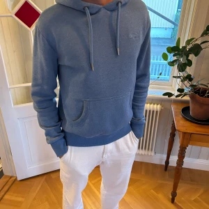 Superdry hoodie - Snygg blå hoodie från Superdry med broderad logga på bröstet. En tjock hoodie som är lite tyngre. Modell är 183cm & 75kg! Bara att skriva om ni har frågor