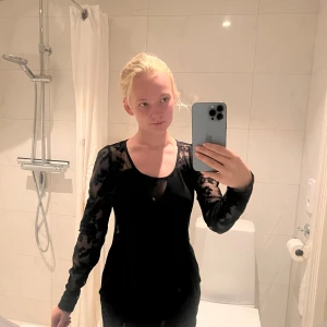 Svart meshblus med spetsdetaljer - Säljer en svart blus med transparenta meshärmar och spetsdetaljer. Blusen har rund halsringning och långärmade ärmar i genomskinligt tyg med blommig spets. Perfekt för dig som vill ha en edgy och stilren look.