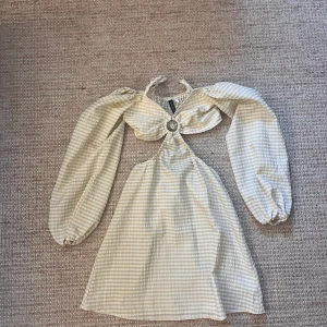 Randig kortklänning med cut out och puffärm - Superfin kortklänning från HM i beige och vitt randigt mönster. Klänningen har långa puffärmar, cut out-detalj framtill med ring och knyt i nacken. Perfekt för dig som vill sticka ut med en trendig och söt look.