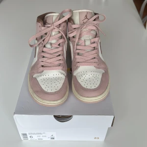 Nike Air Jordan 1 Mid Pink Oxford Brown - Nike Air Jordan 1 Mid i en snygg kombo av ljusrosa, brunt och vitt. Skorna har klassisk snörning, brunt swoosh och detaljer, samt perforerad tåbox. Tillverkade i skinn med en mjuk, vadderad insida och ikoniska Air Jordan-loggan på sidan. Nypris 2199 sek.