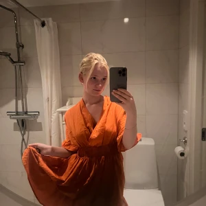 Orange omlottklänning med v-ringning - Säljer en orange kortklänning med omlott och v-ringning. Klänningen har resår i midjan, korta ärmar och ett lätt, flowy tyg som ger en avslappnad vibe. Perfekt för dig som gillar färg och vill sticka ut lite extra.