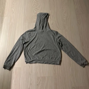 Grå ribbad hoodie från KappAhl - Mysig grå hoodie från KappAhl i ribbad bomullsblandning. Tröjan har huva, långa ärmar och en relaxed passform. Perfekt för chill dagar eller när du vill ha något bekvämt och stilrent. Enkel att matcha med jeans eller mjukisbyxor.