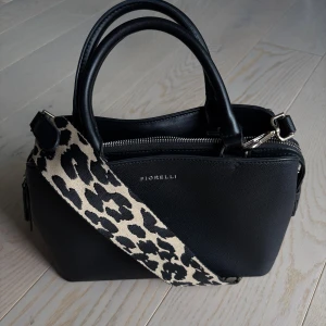 Handväska - Super praktisk handväska i äkta läder från märket Fiorelli. Den är i en mellan storlek och har 3 olika fack. Man kan även byta ut väskbandet💓Den är i väldigt fint skick då jag endast använt den ett fåtal gånger!