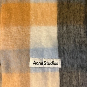 Rutig halsduk från Acne Studios - Supermjuk och fluffig halsduk från Acne Studios i rutigt mönster med färgerna beige, blå, grå och svart. Perfekt oversized modell med fransar i ändarna. Gjord i en lyxig ullblandning som håller dig varm hela vintern.