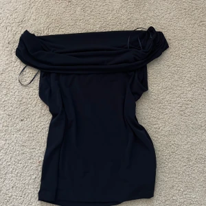 Svart offshoulder klänning Gina Tricot - Snygg svart kortklänning från Gina Tricot med offshoulder-design. Klänningen har en enkel, tight passform och är tillverkad i ett mjukt, stretchigt material som sitter skönt på kroppen. Perfekt för dig som gillar stilrena och trendiga plagg.