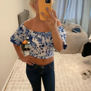 Blommig offshoulder croppad topp - Superfin croppad topp med blått och vitt blommönster. Offshoulder-modell med puffiga korta ärmar🩵