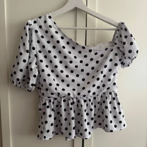 Prickig offshoulder blus med volang - Superfin vit blus med svarta prickar och offshoulder-design. Den är köpt i en butik i Spanien och är i storlek M, men skulle säha att den passar bra på en S.