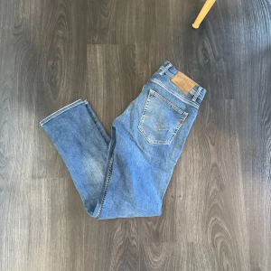 Blå Replay Anbass jeans, storlek 32/32 - Säljer ett par klassiska blå jeans från Replay i storlek 32/32. Jeansen har en snygg tvätt, raka ben och femficksmodell. Materialet är mjukt denim i bomull, perfekt för en avslappnad och stilren look.