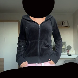 Svart velour hoodie med dragkedja - Mysig svart hoodie i mjuk velour med dragkedja framtill och huva. Jackan har två fickor och ribbade muddar vid ärmslut och nederkant. Perfekt för en chill och avslappnad stil.