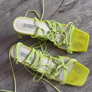 Limegröna sandaler med snörning - Trendiga sandaler i limegrönt med fyrkantig tå och långa snören att knyta runt vristen. Snygg mockaliknande yta framtill och platt sula. Perfekta för att lyfta sommarlooken med en poppig färg.