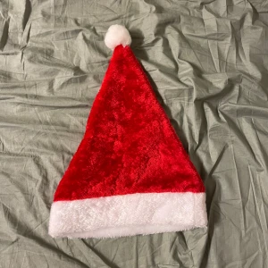 Röd och vit tomteluva i syntet - Klassisk tomteluva i röd och vit plysch med fluffig vit kant och boll på toppen. Perfekt för att maxa julkänslan! Tillverkad i mjukt syntetmaterial som är skönt att bära hela kvällen.