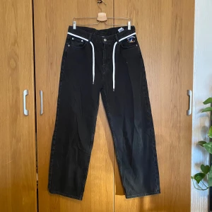 Svarta skate jeans från Cava Company - Svarta skate jeans från Cava Company med broderad detalj på fickan och vita snören i midjan. Rak och baggy passform. Använda en gång så praktiskt sätt nyskick. Nypris: 799kr